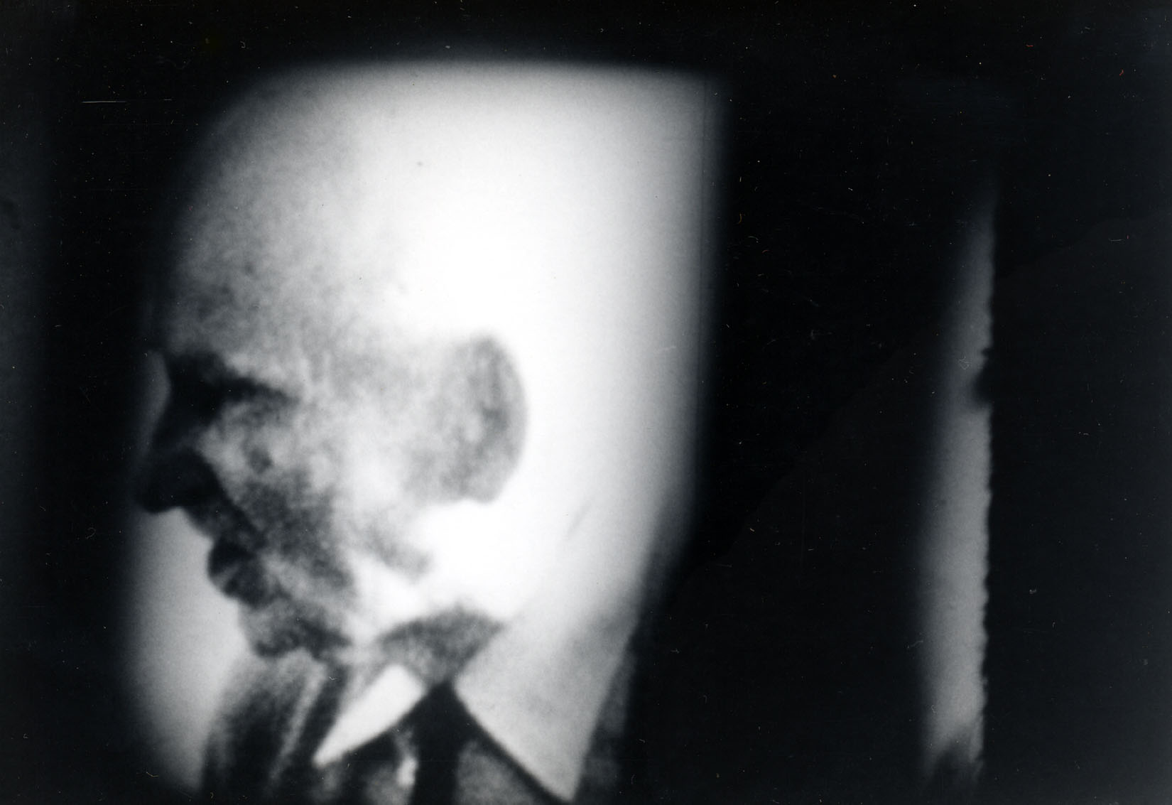 b/w photo of a profile of a man's face, shrowded by black extending from the sides of the frame