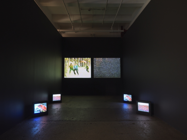 dark room with 4 monitors on ground and 2 video projections: one with man being chased, the other with static