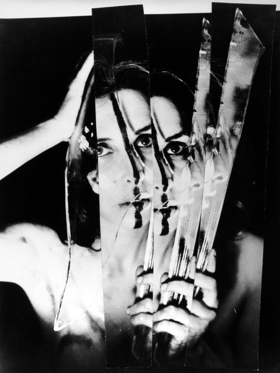 Black and white portrait of the artist holding mirror shards so that her face is reflected in them multiple times, extending to the right.