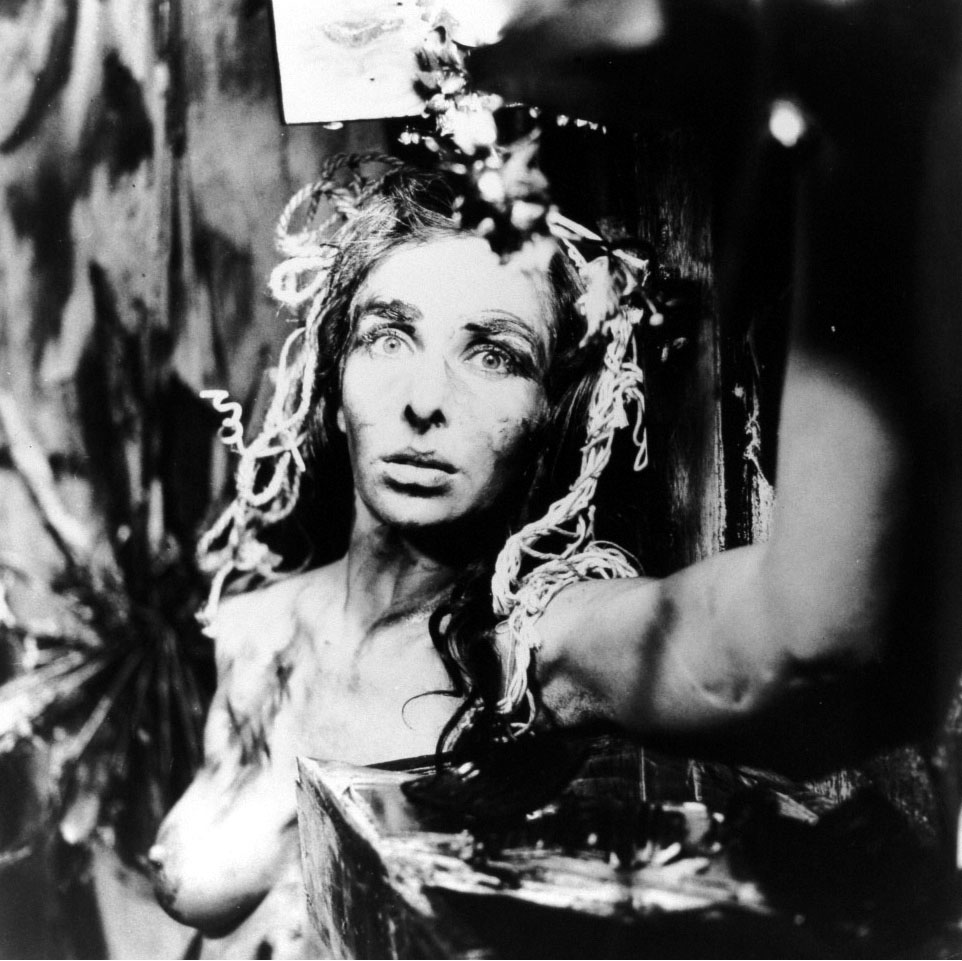 Black and white photo of artist naked, taken from the chest up. Her gaze is up, and there is an arm intruding into the photograph from the right.