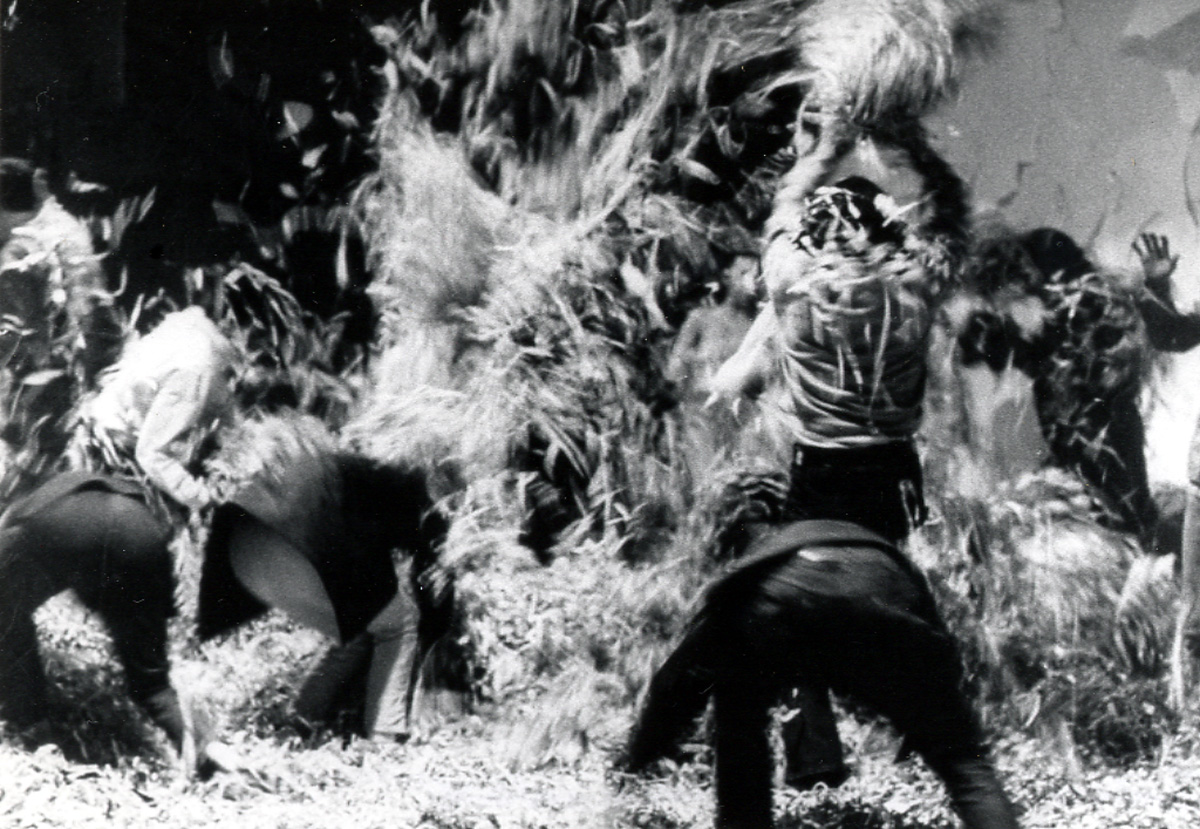 black and white image of many bodies engaged in a playful fight, with feathers and other debri flying around them