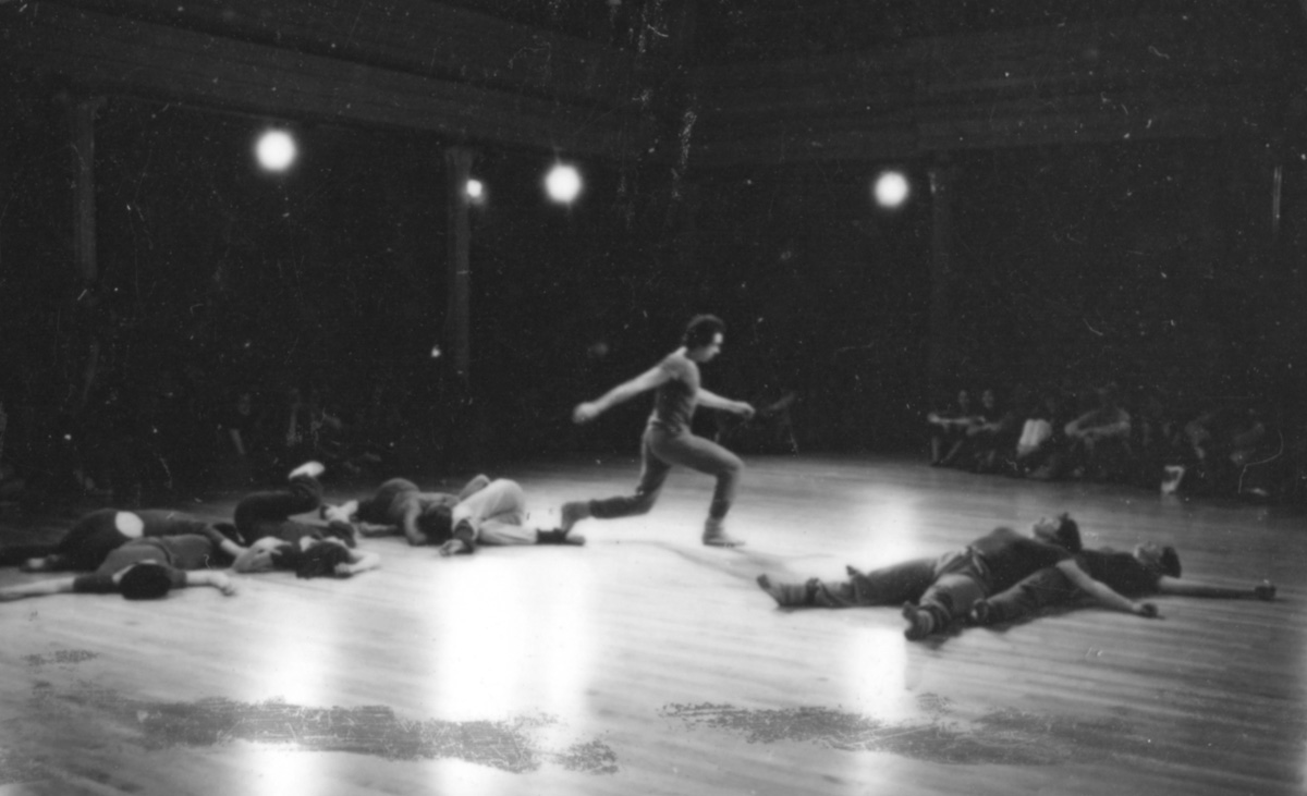 b/w photo of several figures laying on the ground on their sides or back; in the center there is a profile of a figure in lunging position