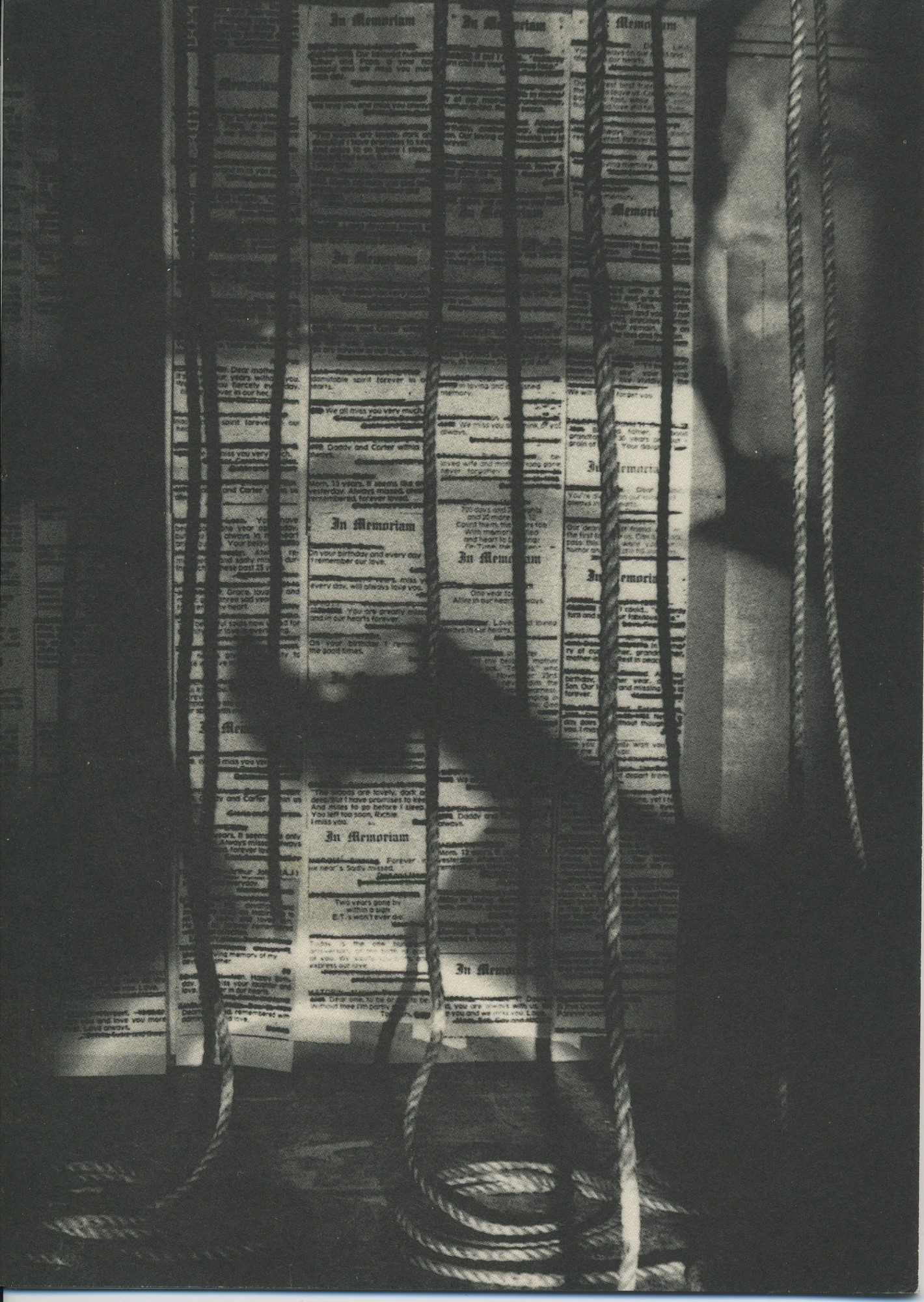 strips of in memorium collumns are pasted to the back wall, with rope hanging in front; from the right, a face enters the scene and casts a shadow over the papers.