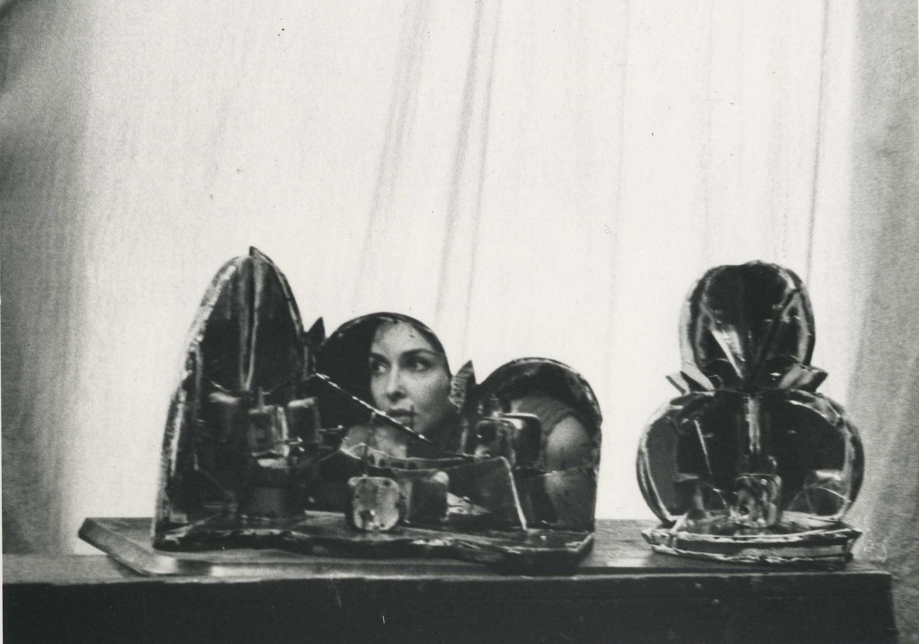 two shattered-glass and music box crank structures in front of a white curtain; Carolee's face is reflected in the works