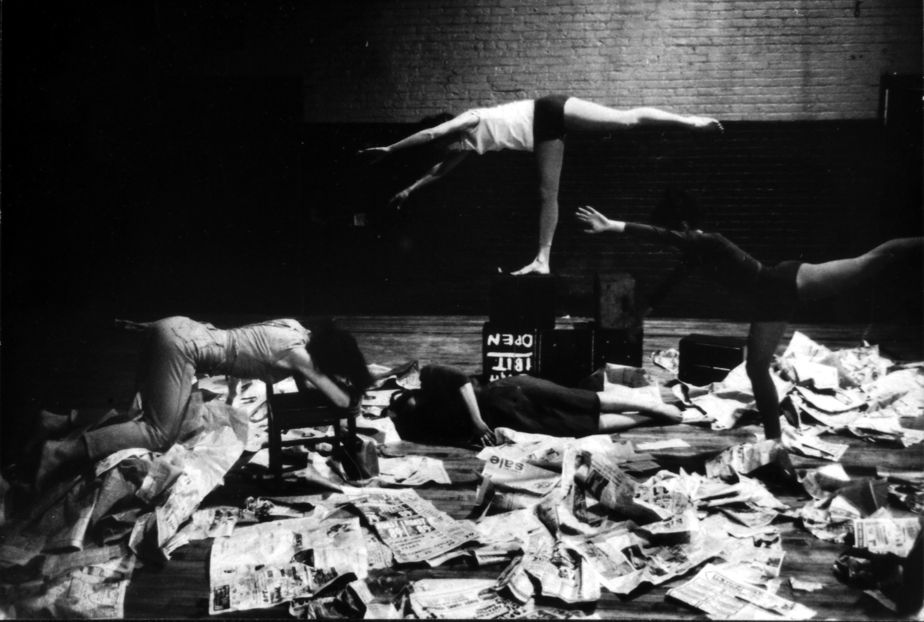 b/w photo of 4 dancers bending and crawling amidst a floor strewn with newspapers