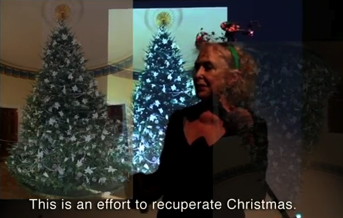 A woman with blonde hair, a black shirt, and a green headband stands in front of two Christmas Trees. The caption reads 'This is an effort to recuperate Christmas.'