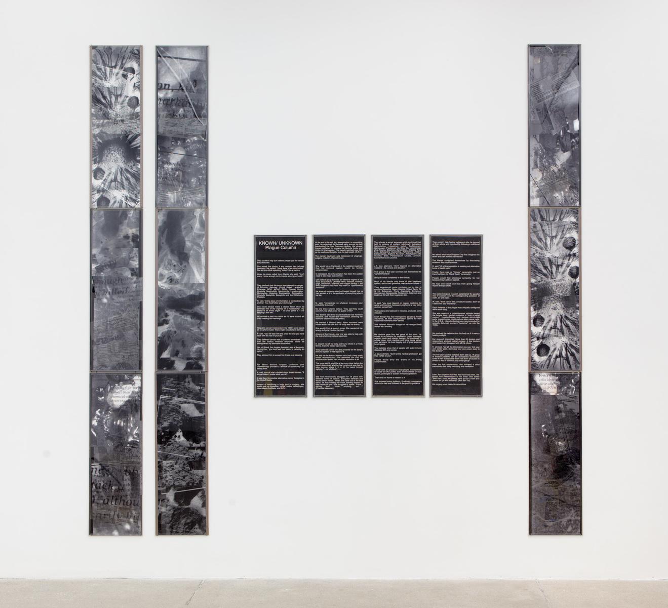 installation shot; in the center are four black panels with white text; to the right are 2 long narrow panels with black and white collages, and another of these panels to the right