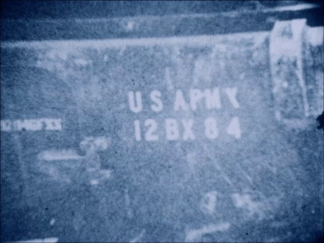 collage image; at the forground is a figure laying face down, bound at the ankles; behind that is an image of a vast army marching; overlaying both is a pink filter with elements reminiscent of the american flag