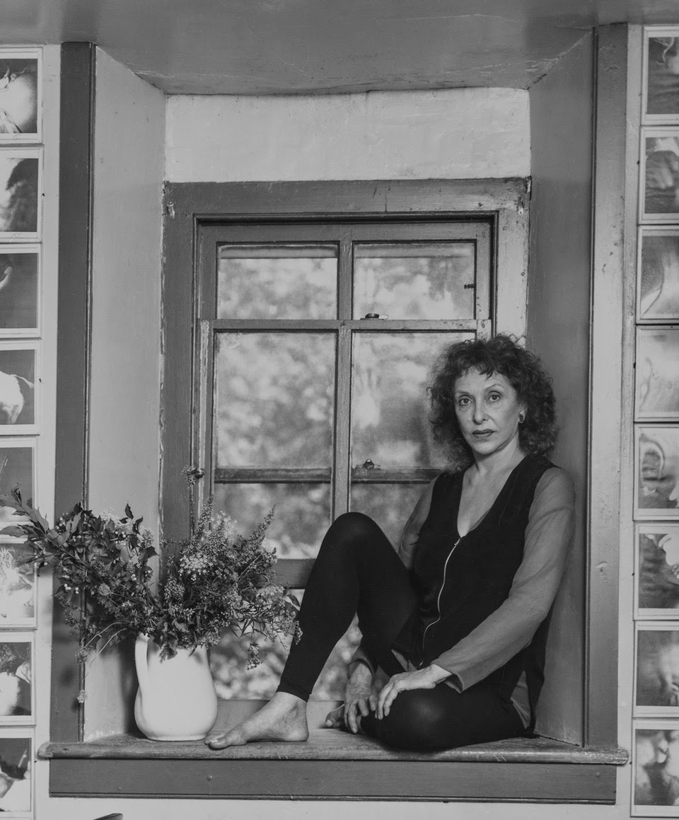 b/w photo of the artist sitting on a windowsill next to a vase of flowers